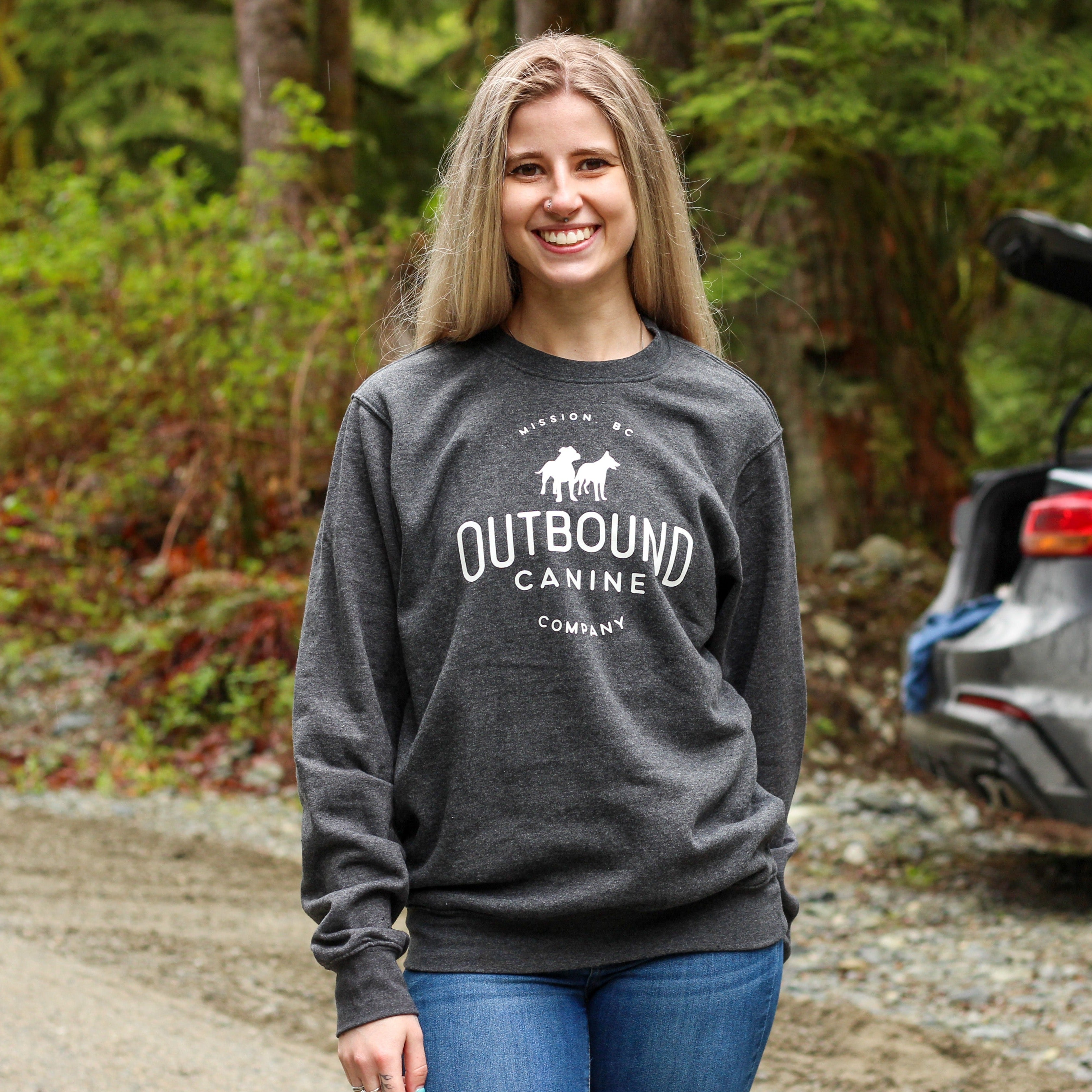 woman smiling at the camera modeling an outbound canine grey crewneck